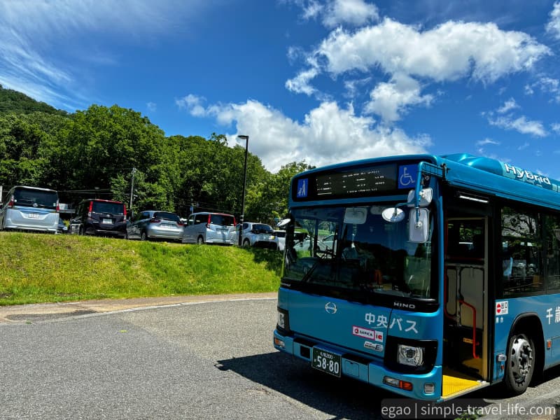 支笏湖バス停に停まる水色の中央バスと、木々に囲まれた駐車場
