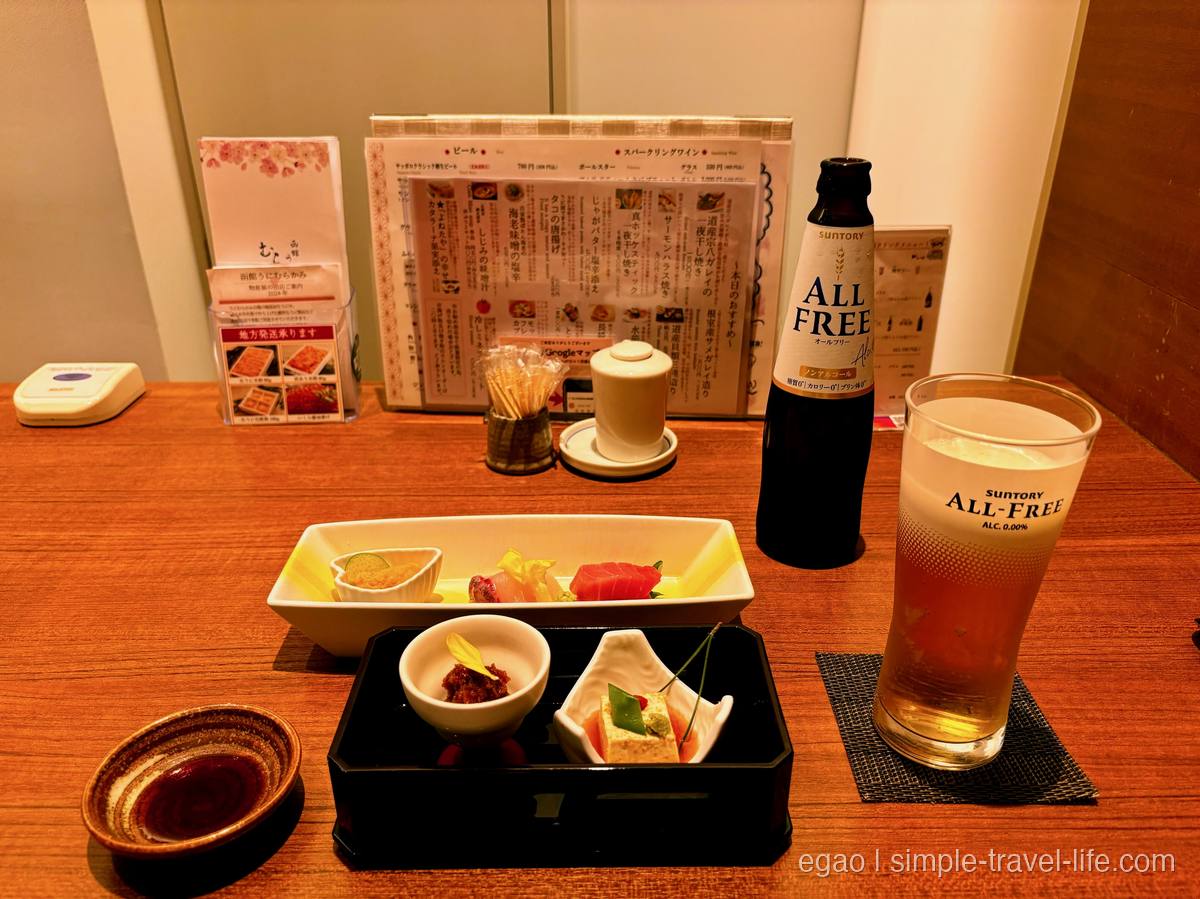 うにと刺身が並ぶ前菜の盛り合わせ。左の小鉢にきゅうりを添えた生うにと、右にノンアルコールビールの瓶とグラス