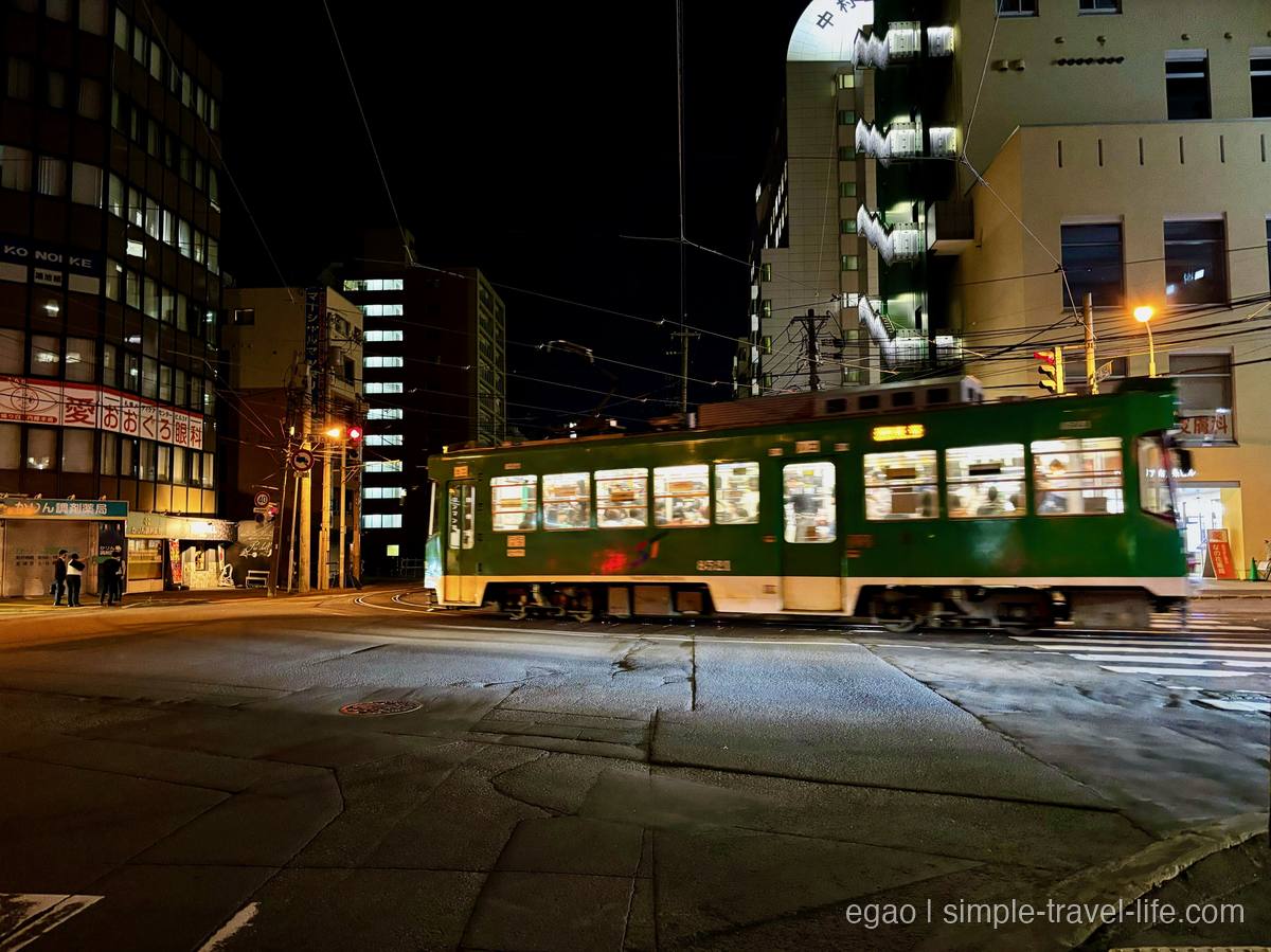夜の交差点を横切る、緑と白の車体の札幌市電