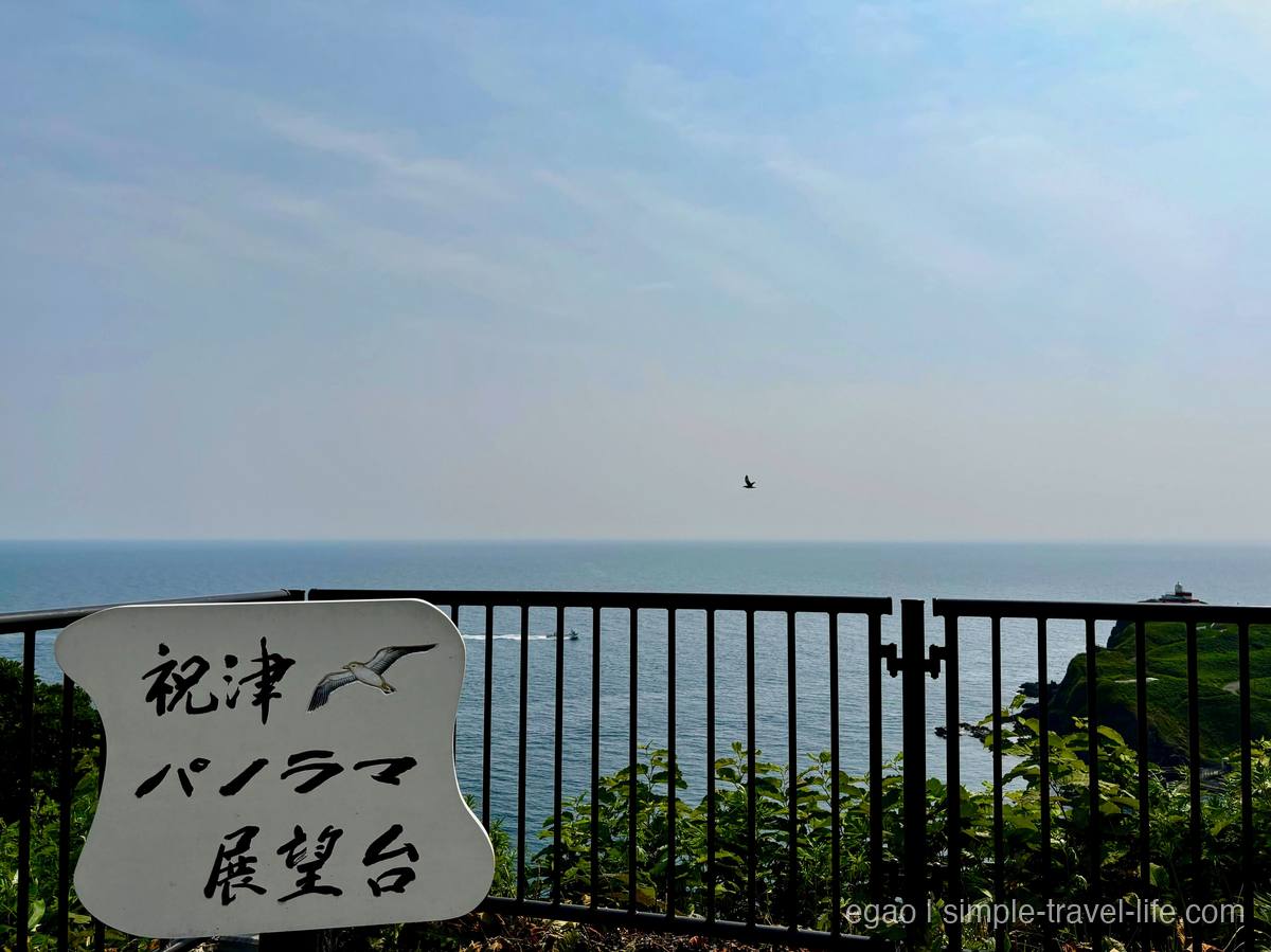 カモメの絵が描かれた「祝津パノラマ展望台」の看板と、柵の向こうに広がる青い海