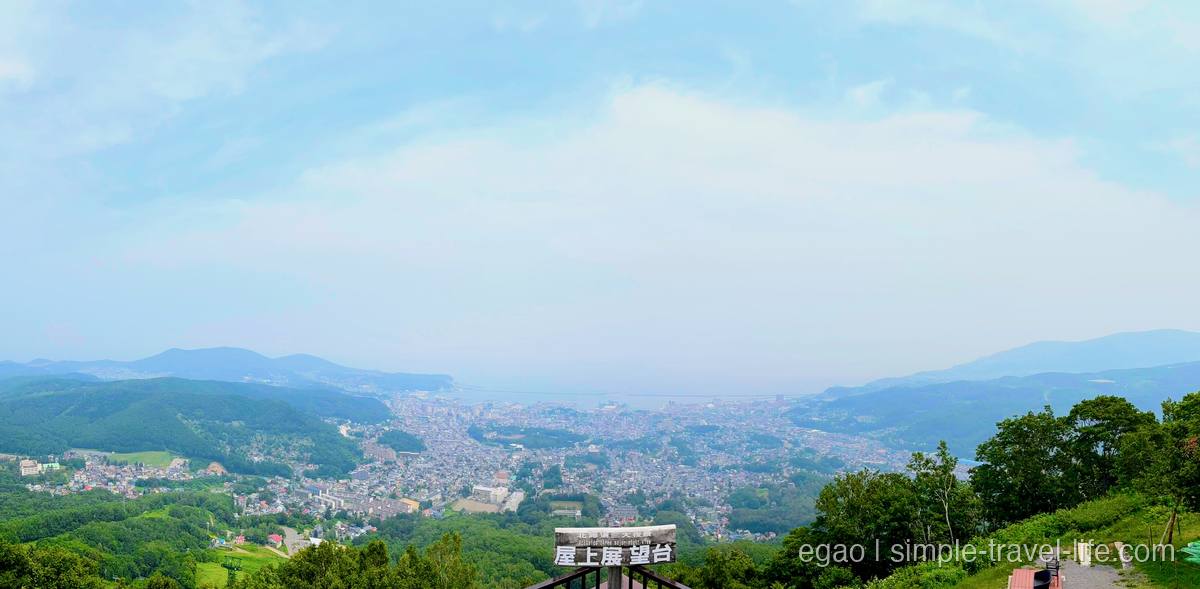天狗山の展望台から見下ろす小樽の市街地と石狩湾のパノラマ、手前に「屋上展望台」の木の看板