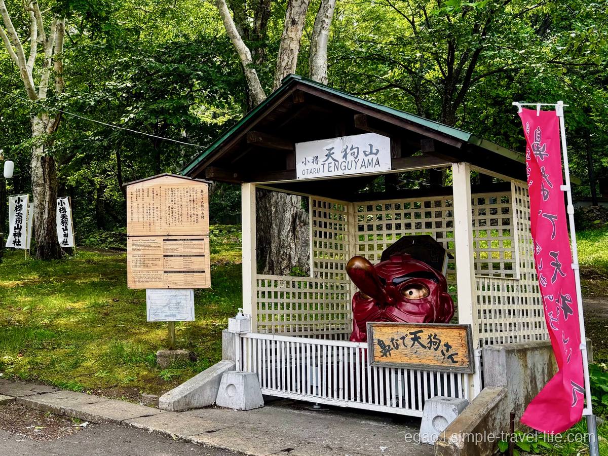 木造の祠に納められた赤い天狗の面と、「鼻なで天狗さん」と書かれた木の看板