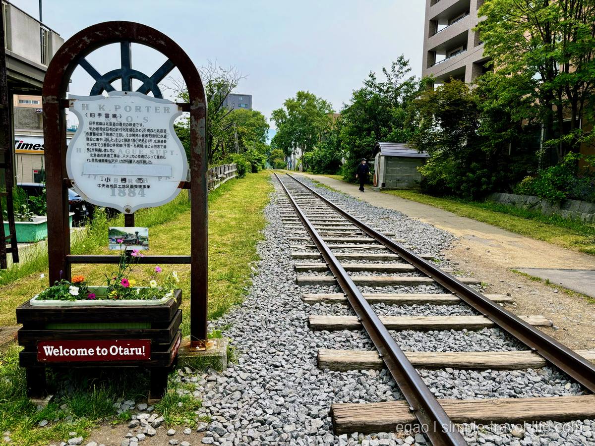 旧手宮線の線路跡にまっすぐ伸びるレールと枕木、手前に「Welcome to Otaru!」の赤い看板と花壇