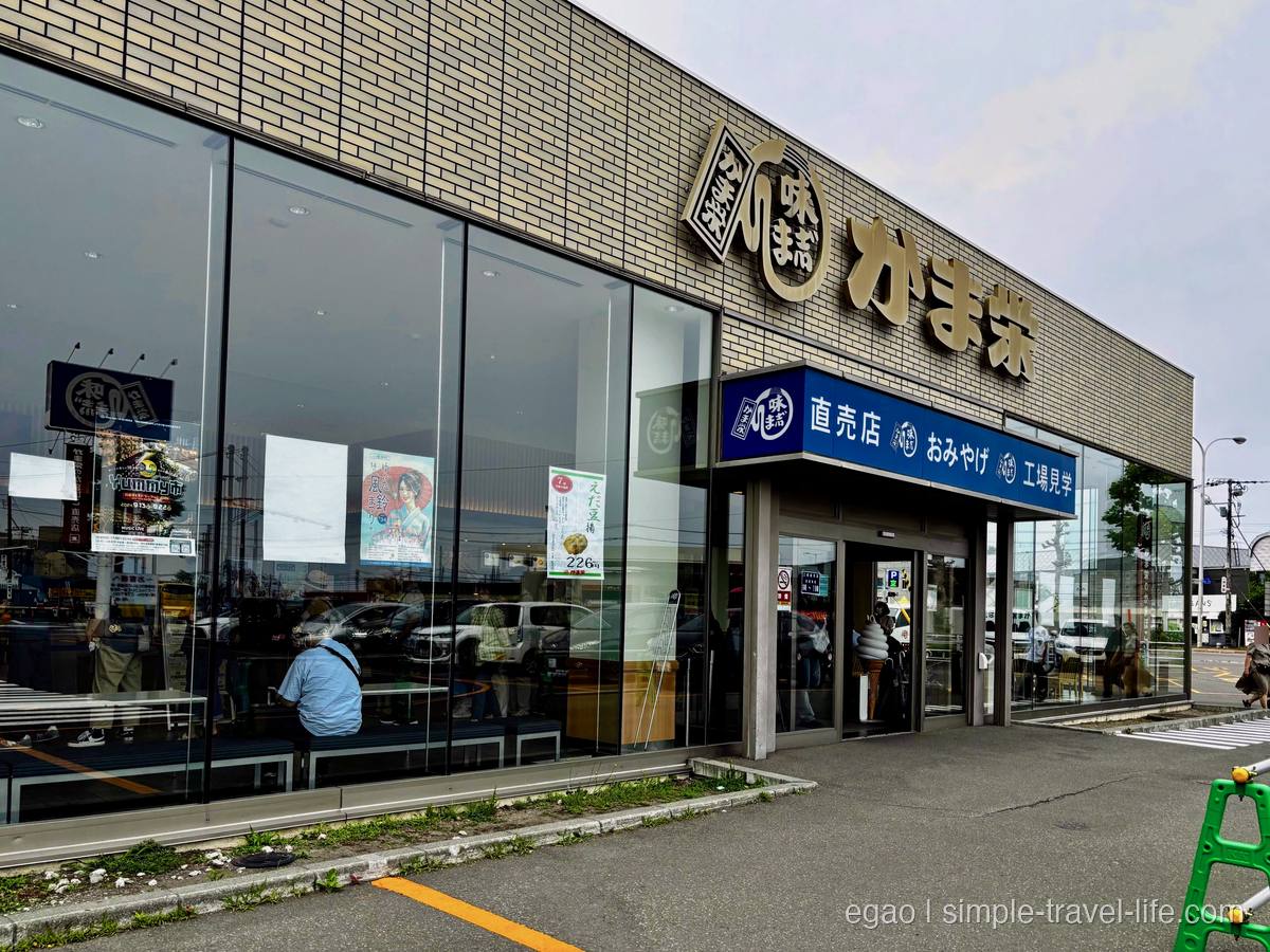 「かま栄」の金文字の看板と、「直売店 おみやげ 工場見学」と書かれた青いひさしのガラス張りの店舗