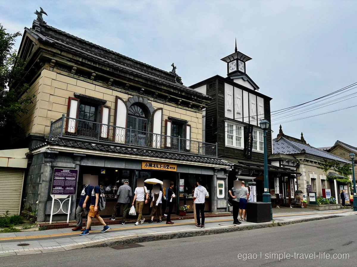 瓦屋根の石造りの建物に「小樽オルゴール堂 本館」の看板が掲げられた店先と、隣に立つ時計塔