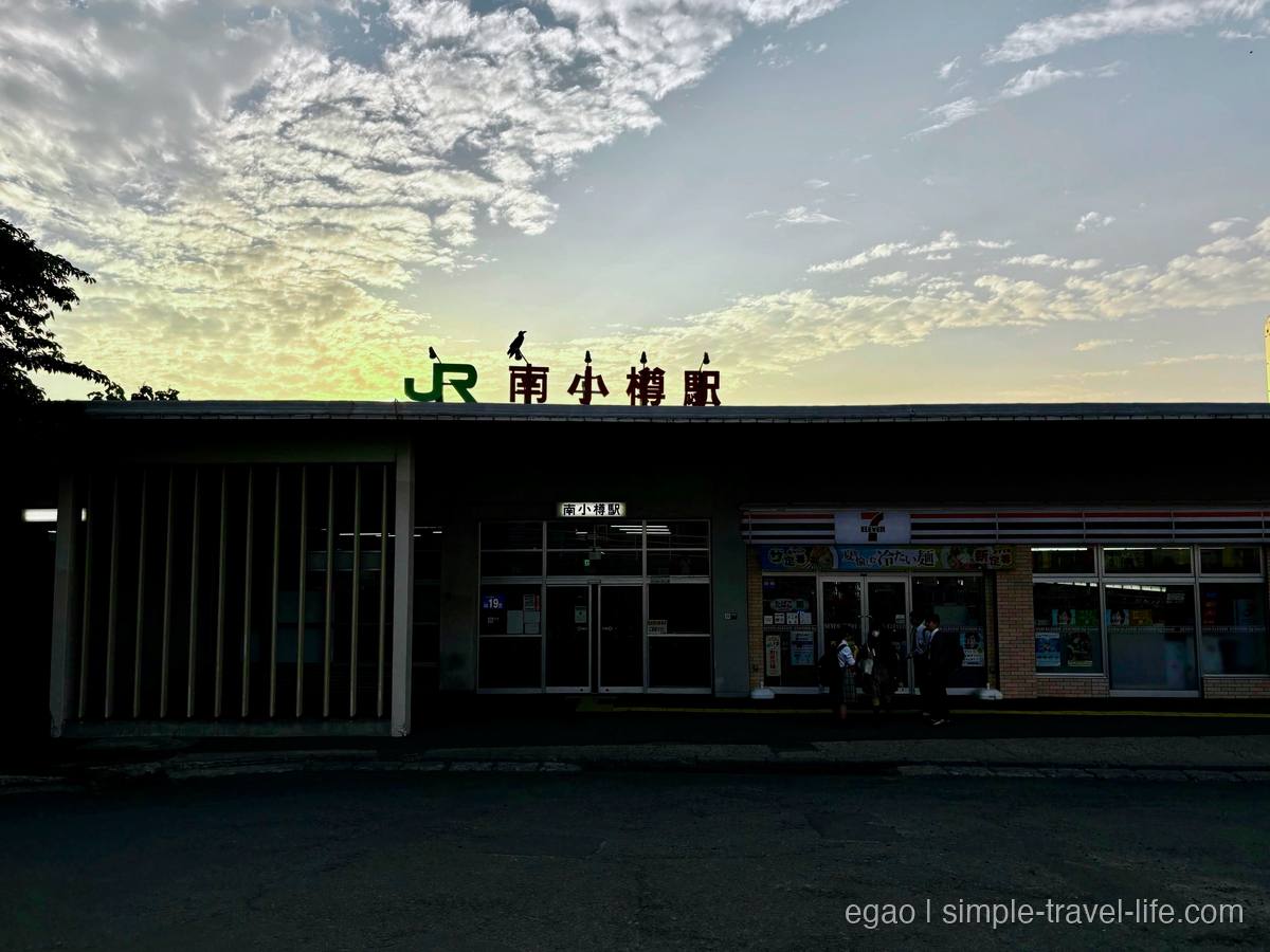 夕暮れの空の下、屋根に「JR南小樽駅」の文字が掲げられた駅舎
