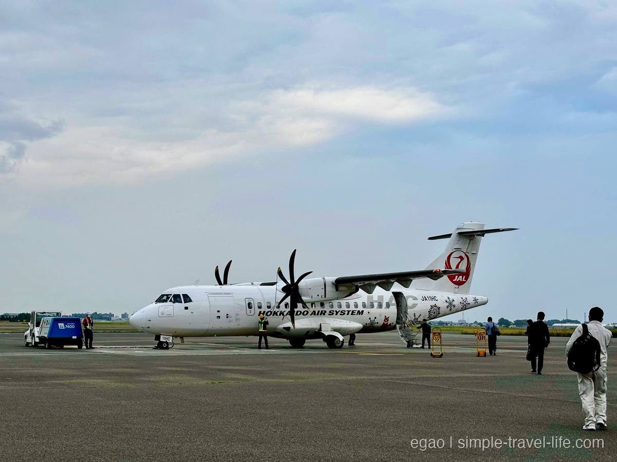 駐機場に停まる北海道エアシステムの白いプロペラ機と、機体へ歩いて向かう乗客