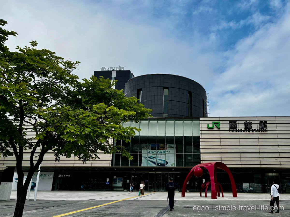 ガラス張りの外観に「JR函館駅」の文字が並ぶ函館駅と、駅前広場の赤いオブジェ