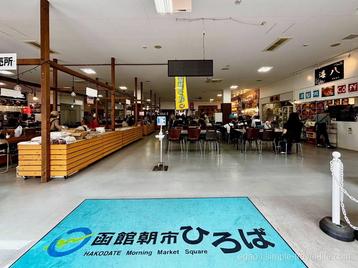 床に「函館朝市ひろば」のロゴが入った館内と、奥に並ぶ飲食店とフードコートの席