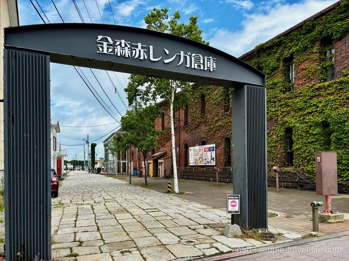 「金森赤レンガ倉庫」と掲げられた黒いアーチ型ゲートと、その先に続く石畳とレンガ倉庫