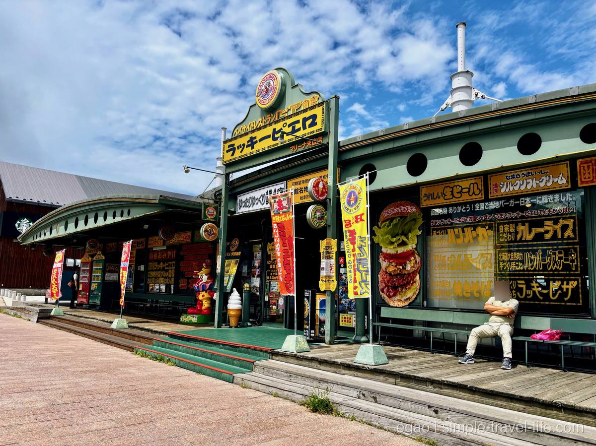 黄色いのぼりと看板が並ぶ「ラッキーピエロ マリーナ末広店」の緑色の店構え