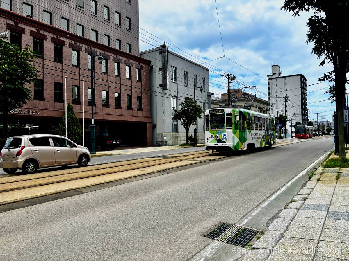 函館の街なかの併用軌道を走る緑と白の函館市電と、後続の車両