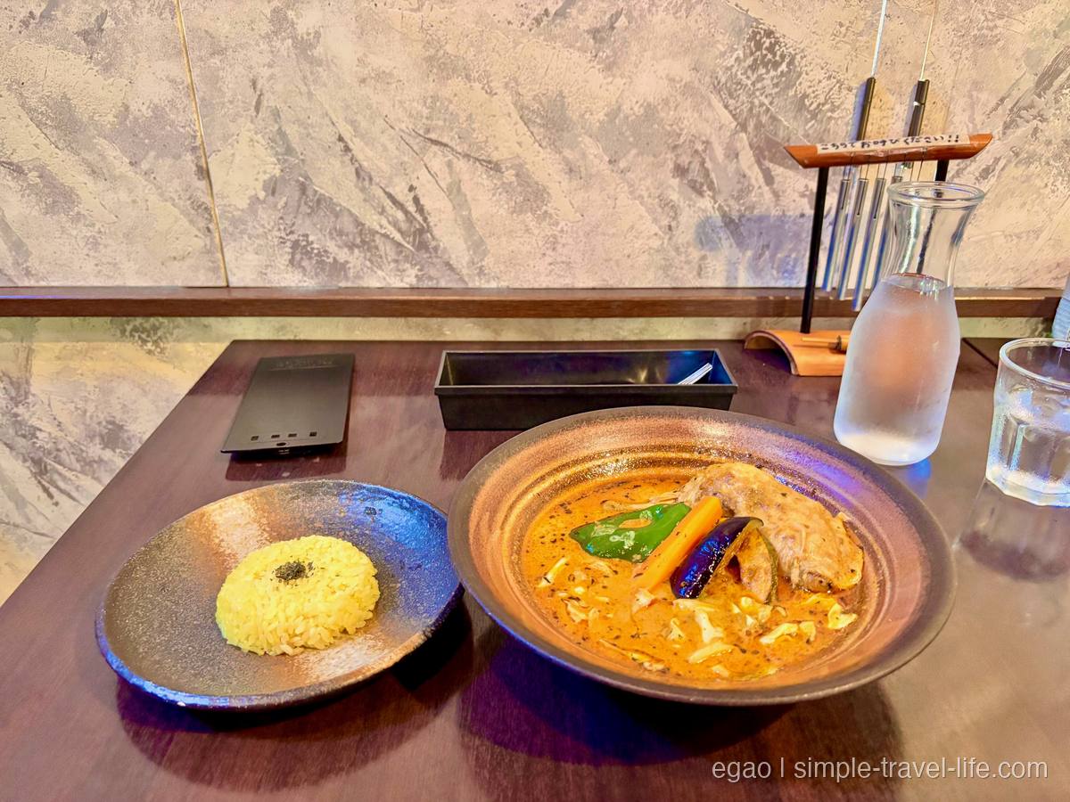 オレンジ色のスープカレー。ピーマン、にんじん、なす、大ぶりの鶏肉が入り、別皿に黄色いライス
