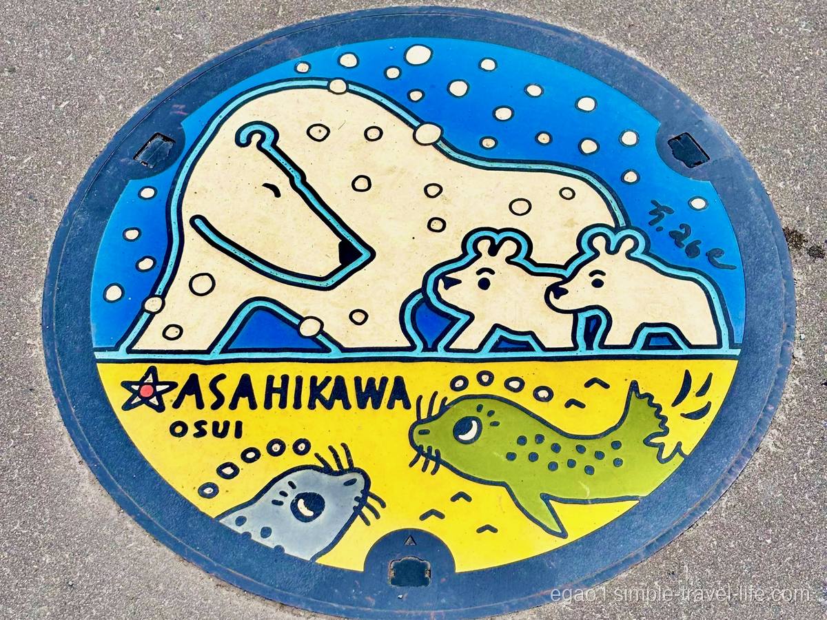 マンホールのふた。上半分に雪の中を歩くホッキョクグマの親子、下半分に2頭のアザラシと「ASAHIKAWA OSUI」の文字