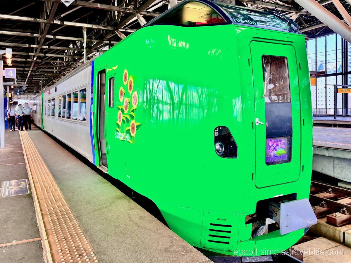 ホームに停まる鮮やかな緑色の特急車両。先頭部の側面にひまわりの絵と「SORACHI」の文字、うしろは銀色の車体