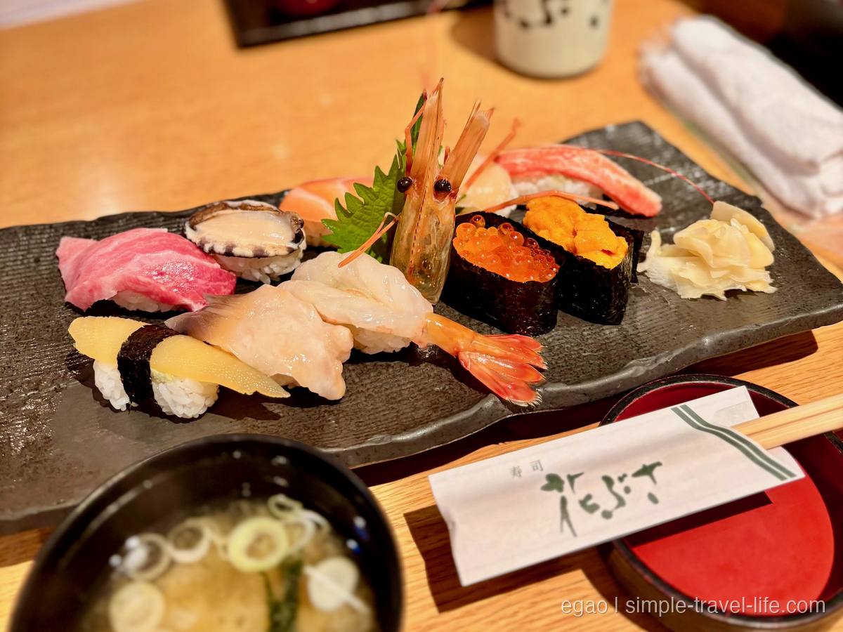 黒い石の皿に並ぶにぎり寿司。まぐろ、貝、サーモン、かに、頭つきの甘えび、いくらとうにの軍艦、ガリ。手前に味噌汁の椀